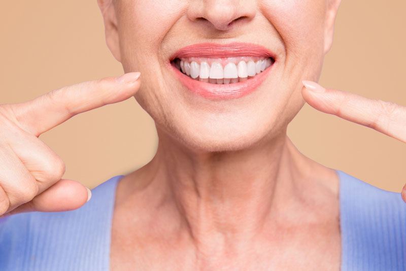 Smiling senior woman pointing at her dental implants and healthy teeth after cosmetic dentistry treatment