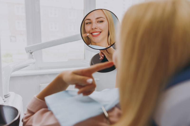 2025-07-NP1 Young smiling satisfied fun happy calm woman 20s reflected in mirror sitting at dental office